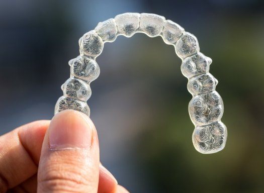 Hand holding an Invisalign aligner outdoors