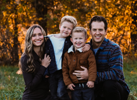 Doctor Liz smiling outdoors with her husband and two sons